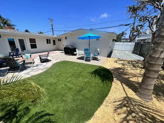 Backyard with artificial turf lawn, palm trees, a blue patio umbrella and lounge chairs