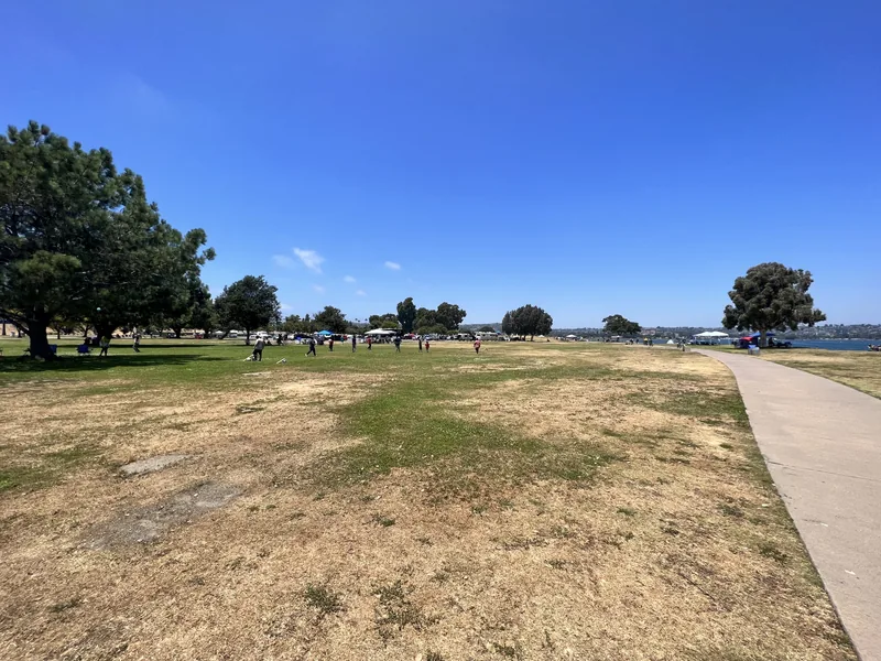 Grassy bayfront park with picnic tables and a paved path running along Mission Bay