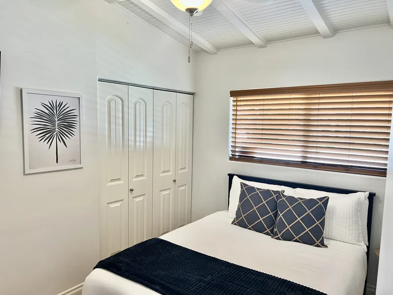 Second bedroom with a queen bed in navy and white linens, a closet and window blinds