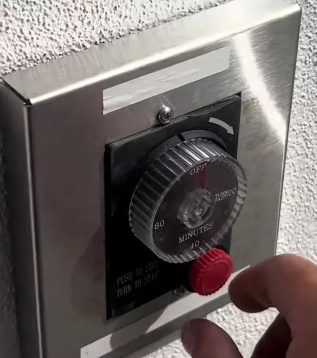 The stainless panel on the patio wall showing a black timer knob marked OFF, 20, 40 and 60 minutes, with a red push-to-stop button beside it