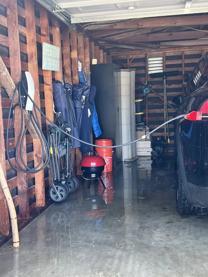 Garage with bikes, strollers, paddles and beach gear stored along the wall beside a parked car