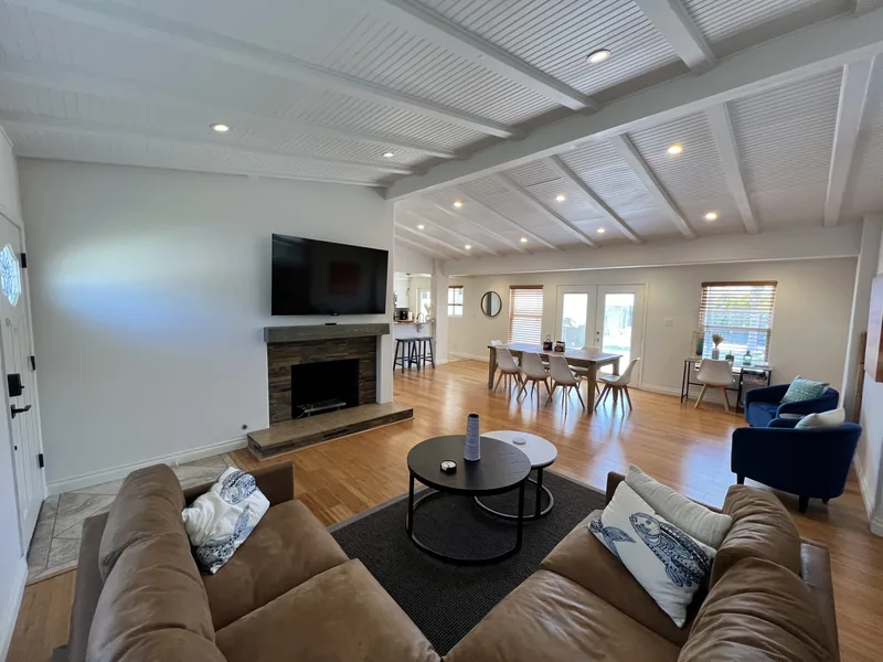 The great room looking toward the kitchen, with a gas fireplace, wall-mounted TV, dining table and French doors to the backyard