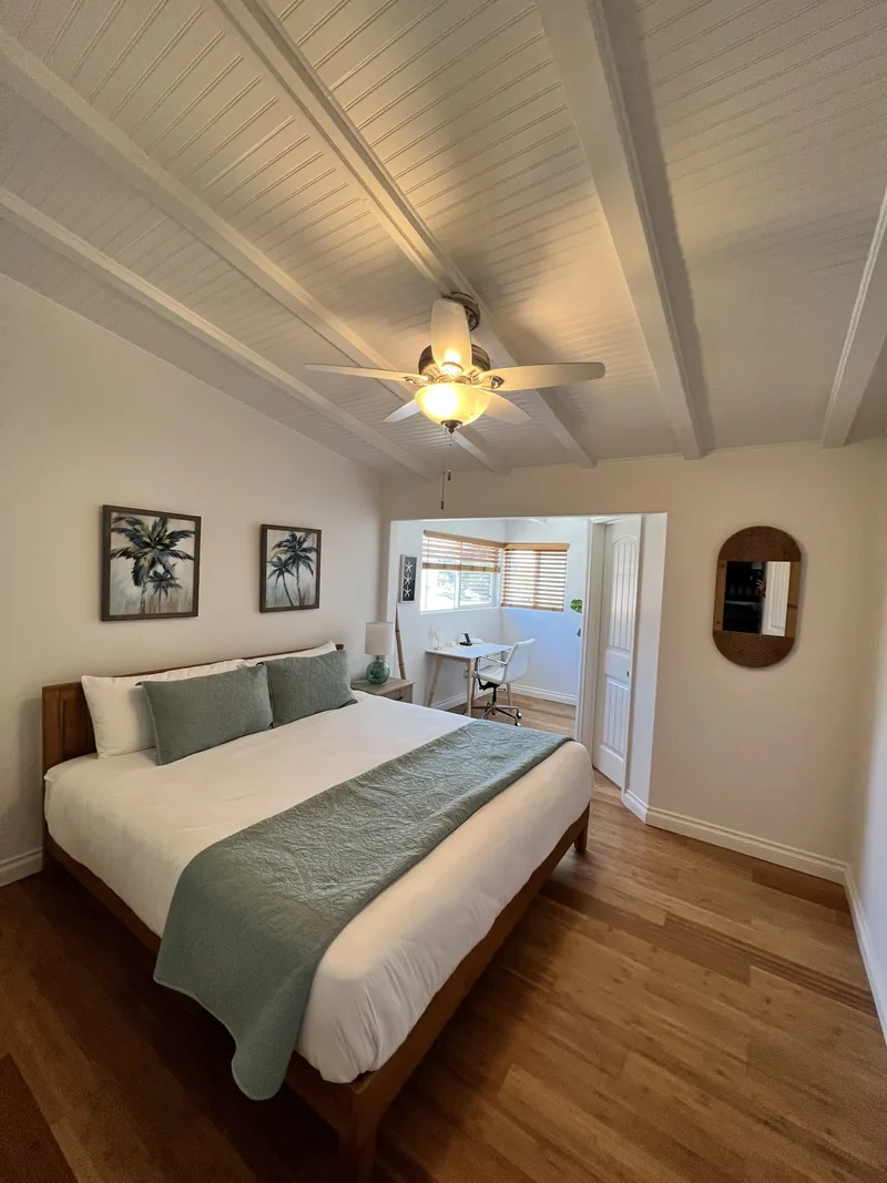 Master bedroom with a queen bed in sage green linens, vaulted ceiling with a fan, and a doorway through to the bathroom