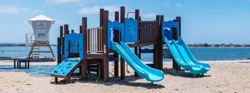 The Fanuel Street Park play structure on the sand, with a lifeguard tower and the bay behind