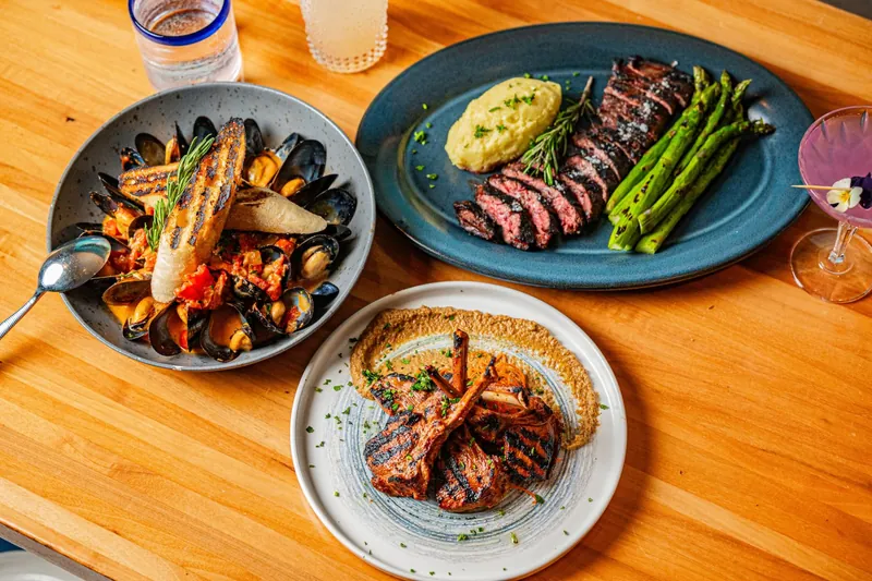 Steak, lamb chops and a bowl of mussels laid out on a wooden table at JRDN