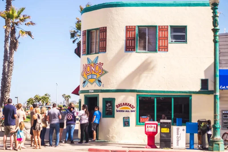 The Kono’s Cafe corner building on Ocean Front Walk, palm trees above and a line of people waiting at the door