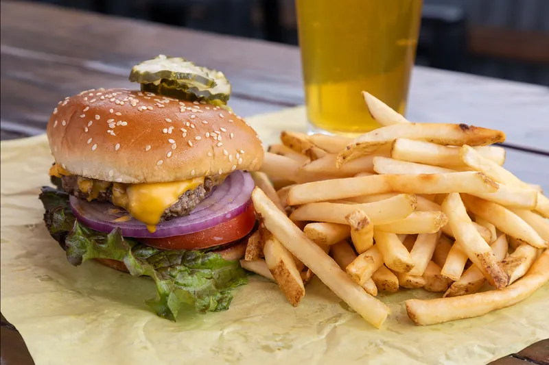 A cheeseburger with lettuce, tomato, red onion and a pickle on top, with fries and a beer, on the bar at Rocky’s