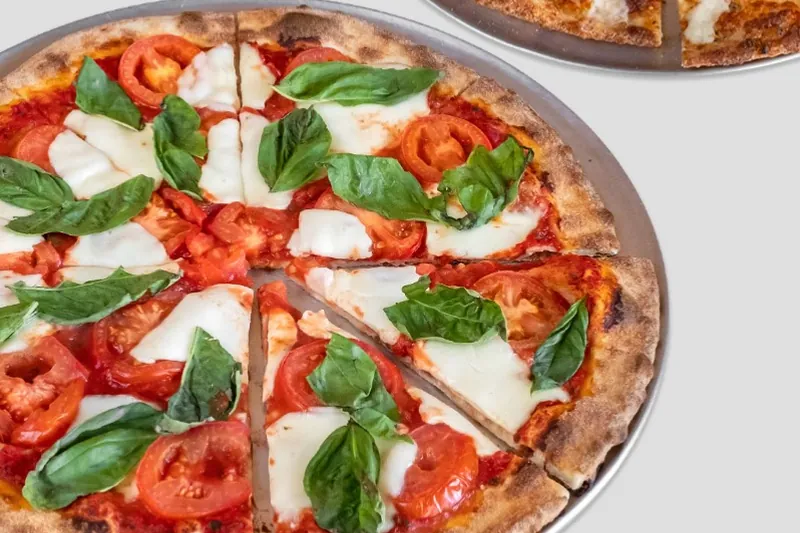 A margherita pizza with fresh basil and a cheese pizza on trays from Theo’s Hot Pizza