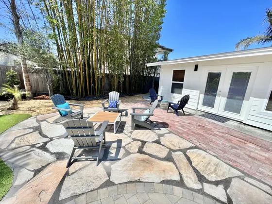 Backyard flagstone patio with a round white gas fire pit and Adirondack chairs
