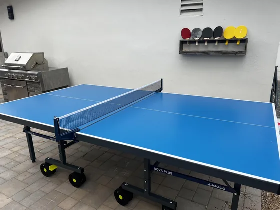 Blue ping pong table set up with paddles hanging on the wall behind