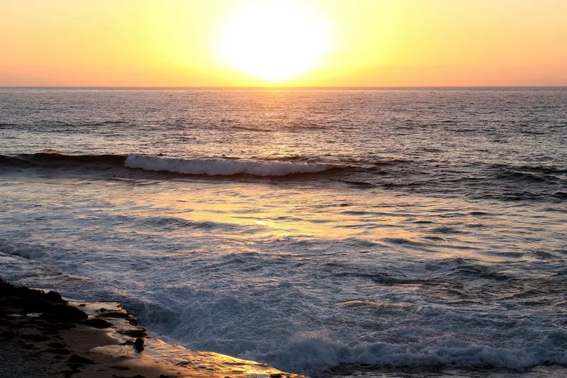 The sun dropping towards the water beyond the sandstone cliffs at Sunset Cliffs