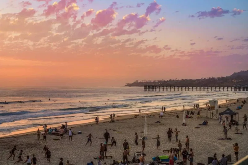 The beach at sunset with Crystal Pier in silhouette against an orange sky
